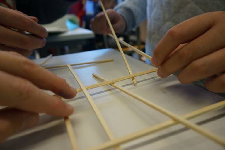 Kinderhände nutzen Holzspieße für Gitternetz